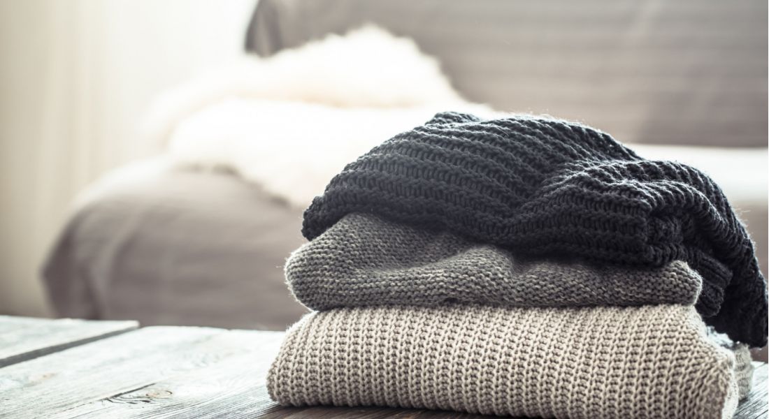 The Wade Three colorful sweaters neatly stacked on top of each other, showcasing different textures and styles.
