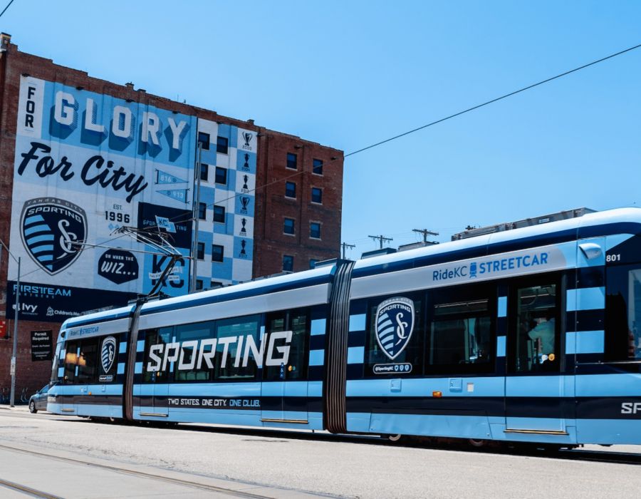 The Wade A blue and white tram travels along a city street, surrounded by buildings and trees.