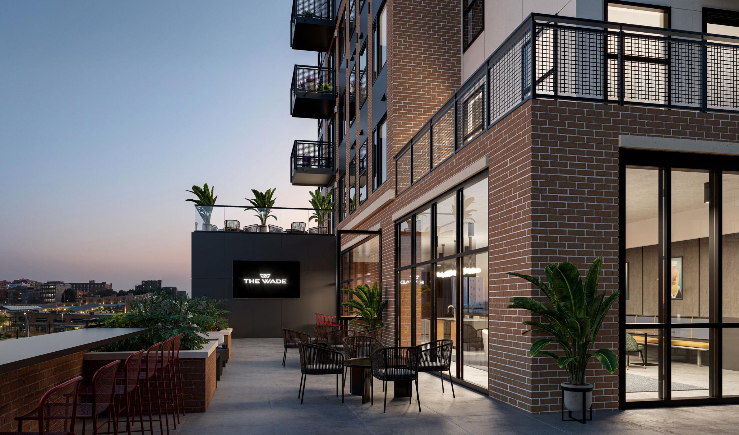 The Wade Rooftop patio of a new apartment building featuring seating areas and greenery with a city skyline view.