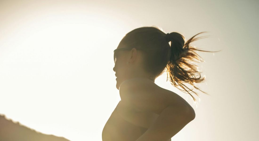 The Wade A woman runs on a sunlit hill, showcasing her athleticism against a bright blue sky.